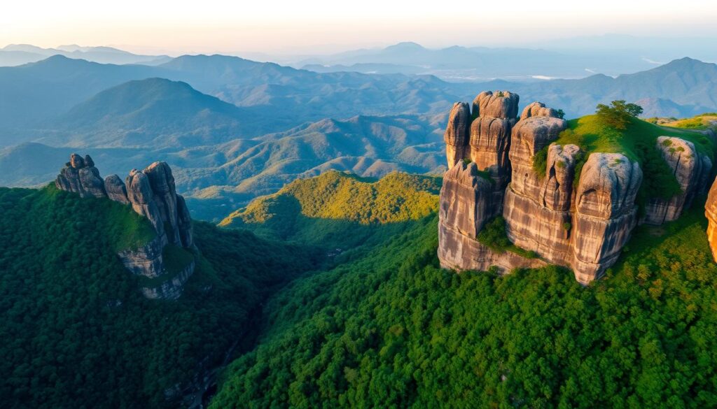 A breathtaking aerial view of the Konkan Kada, a dramatic cliff formation overlooking the rugged Sahyadri mountains. The foreground showcases the towering, jagged limestone cliffs, bathed in warm golden light from the setting sun. In the middle ground, lush green forests cascade down the slopes, contrasting with the grey rocky outcrops. The background reveals the vast, undulating landscape of the Western Ghats, with distant blue-hued peaks fading into the horizon. The scene exudes a sense of scale, power and timeless beauty, capturing the magnificent Konkan Kada in all its splendor.